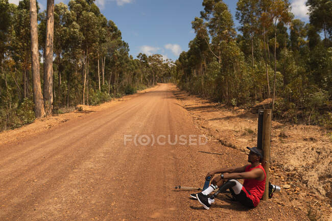 A fit, disabled mixed race male athlete with prosthetic leg, enjoying his time on a trip, hiking, sitting on a dirt road in a forest. Active lifestyle with disability. — Stock Photo