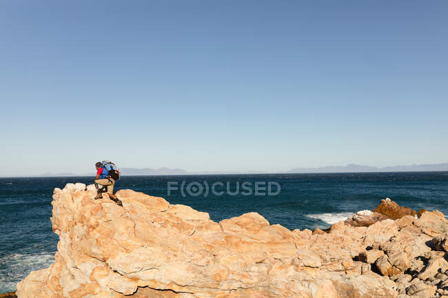 Athlète masculin de race mixte en forme et handicapé avec une jambe prothétique, profitant de son temps sur un voyage à la montagne, randonnée, escalade sur les rochers par la mer. Mode de vie actif avec handicap. — Photo de stock