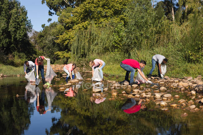 Groupe multiethnique de bénévoles de la conservation qui nettoient les rivières à la campagne, ramassent les ordures. Écologie et responsabilité sociale en milieu rural. — Photo de stock
