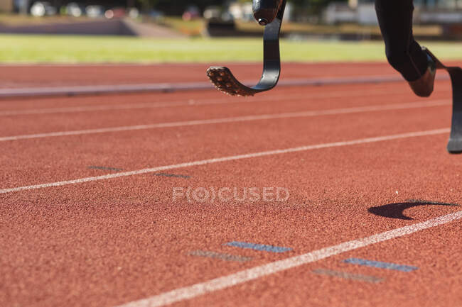 Low section section of fit, disabled male athlete at an outdoor sports stadium, running on race track on running blades. Disability sport training. — Stock Photo