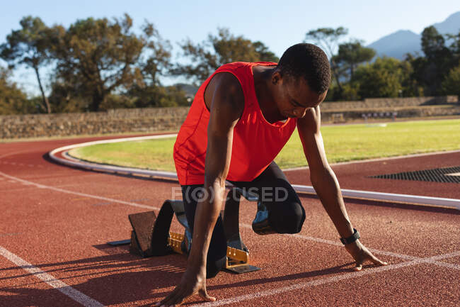 Fit, gemischt rennbehinderter männlicher Athlet in einem Outdoor-Sportstadion, kniet mit Laufschuhen in den Startlöchern auf der Rennstrecke. Behindertensport. — Stockfoto