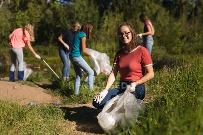 Портрет кавказької жінки - добровольця, що очищає ріку в сільській місцевості, її друзі забирають сміття на задньому плані. Екологія і соціальна відповідальність в сільському середовищі. — стокове фото