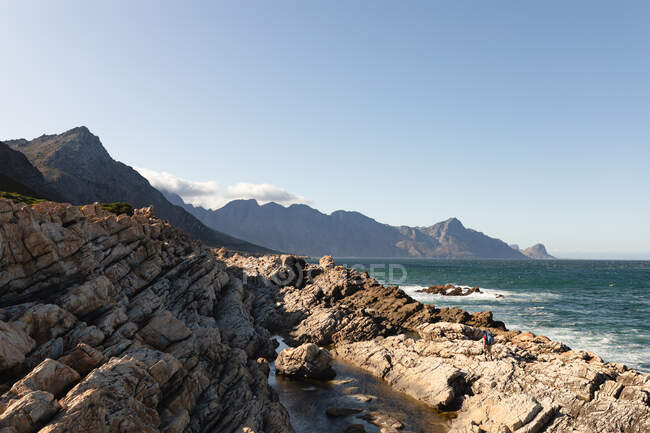 Acantilados costeros rocosos por un mar tranquilo y azul con cielo azul claro en un día soleado. Hermoso paisaje natural junto a la costa. - foto de stock