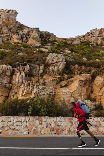 A fit, disabled mixed race male athlete with prosthetic leg, enjoying his time on a trip to the mountains, hiking, walking on the road. Active lifestyle with disability. — Stock Photo