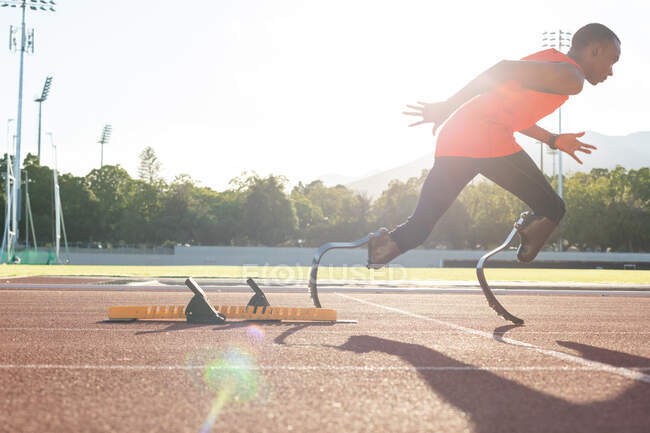 Fit, mixed race disabled male athlete at an outdoor sports stadium, running from starting blocks on race track wearing running blades. Disability athletics sport training. — Stock Photo