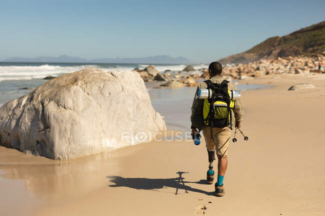 Um atleta masculino de raça mista, apto, com perna protética, aproveitando seu tempo em uma viagem para as montanhas, caminhando com paus, andando na praia à beira-mar. Estilo de vida ativo com deficiência. — Fotografia de Stock