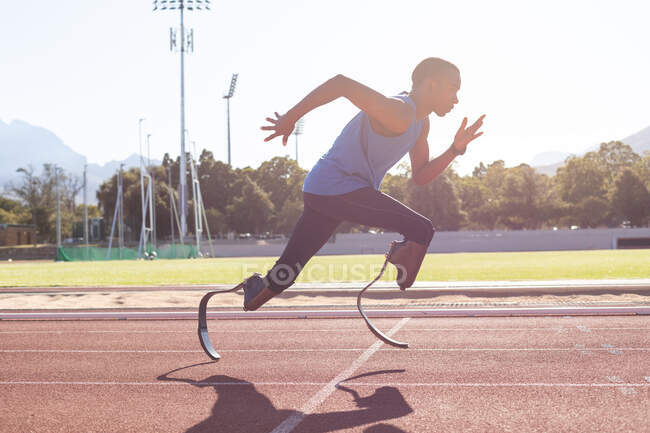 Fit, mixed race disabled male athlete at an outdoor sports stadium, running on race track wearing running blades. Disability athletics sport training. — Stock Photo
