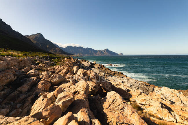 Скалистые прибрежные скалы у спокойного синего моря с ясным голубым небом в солнечный день. Красивые природные пейзажи на побережье. — стоковое фото