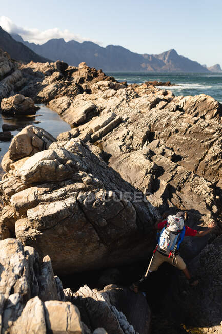 Um atleta masculino de raça mista, apto, com perna protética, aproveitando seu tempo em uma viagem para as montanhas, caminhadas, escalada nas rochas junto ao mar. Estilo de vida ativo com deficiência. — Fotografia de Stock