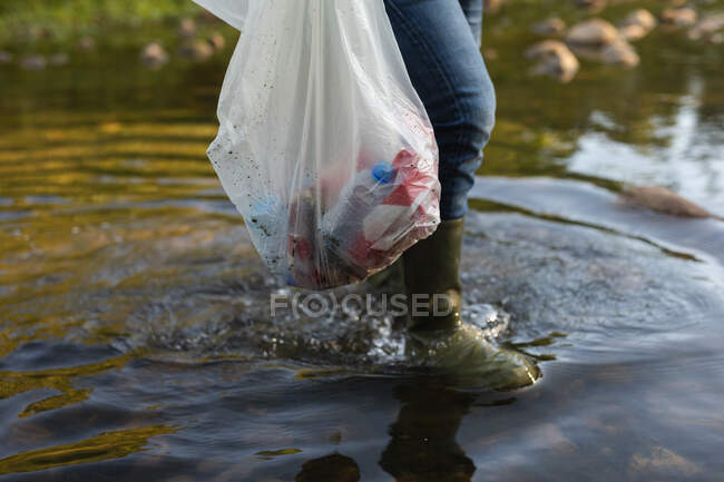 Bassa sezione di volontari di conservazione ripulire il fiume in campagna, portando borsa piena di spazzatura. Ecologia e responsabilità sociale nell'ambiente rurale. — Foto stock
