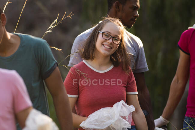 Retrato de una mujer caucásica feliz voluntaria de conservación limpiando el campo, recogiendo basura de sus amigos a su alrededor. Ecología y responsabilidad social en el medio rural. - foto de stock