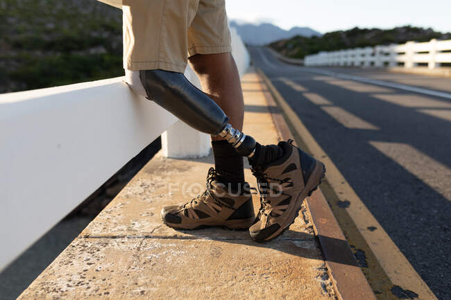 Fitnessarmer, behinderter Sportler mit Beinprothese, der seine Zeit auf einem Ausflug in die Berge, beim Wandern und auf der Straße in den Bergen genießt. Aktiver Lebensstil mit Behinderung. — Stockfoto