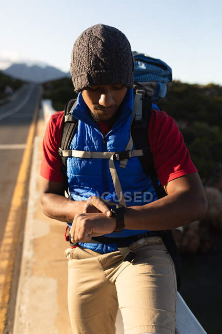 A fit mixed race male athlete, enjoying his time on a trip to the mountains, hiking, taking a break and checking his smartwatch. Active lifestyle mountain hiking. — Stock Photo