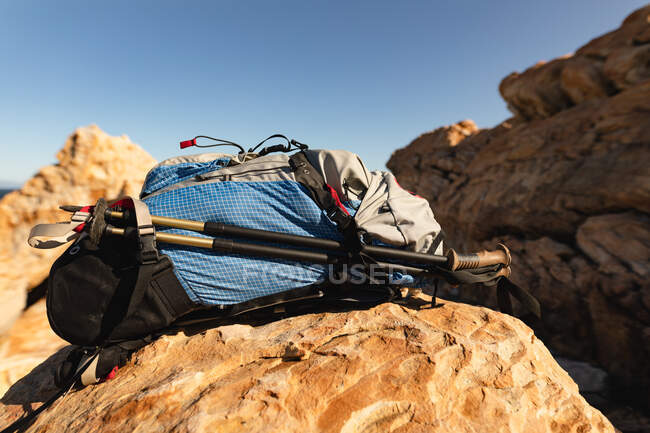 A hikers backpack and Nordic walking sticks sitting on a rock on rocky coastal cliffs with clear, blue sky on a sunny day. Beautiful natural scenery by the coast. — Stock Photo