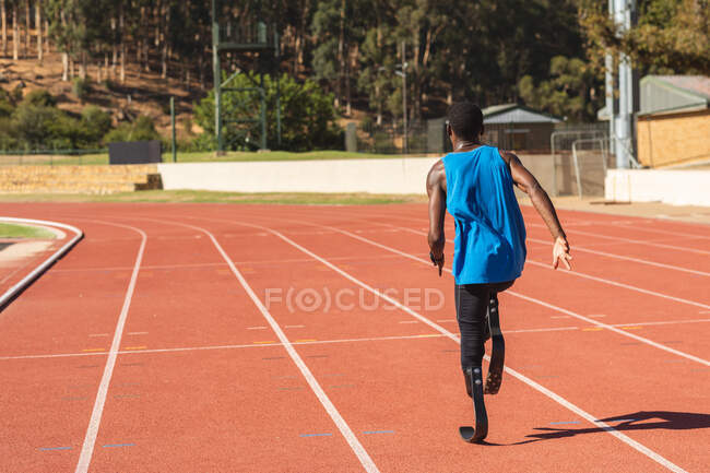 Atleta maschile disabile di razza mista in forma in uno stadio sportivo all'aperto, corre su pista su lame da corsa. Disabilità atletica allenamento sportivo. — Foto stock
