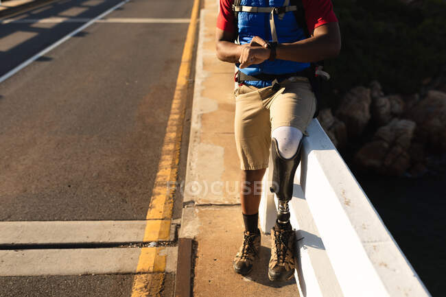 Mid section of a fit, disabled male athlete with prosthetic leg, enjoying his time on a trip to the mountains, checking his smartwatch. Active lifestyle with disability. — Stock Photo
