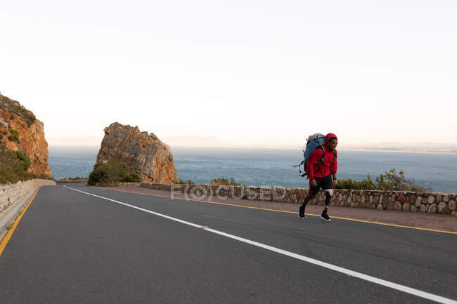 Um atleta masculino de raça mista, apto, com perna protética, aproveitando seu tempo em uma viagem para as montanhas, caminhadas, caminhadas na estrada à beira-mar. Estilo de vida ativo com deficiência. — Fotografia de Stock