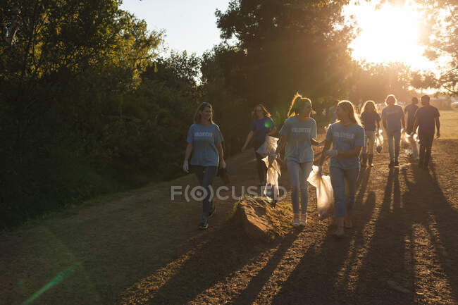 Groupe multiethnique de bénévoles de la conservation qui nettoient la forêt à la campagne, marchent en tenant des sacs poubelles. Écologie et responsabilité sociale en milieu rural. — Photo de stock