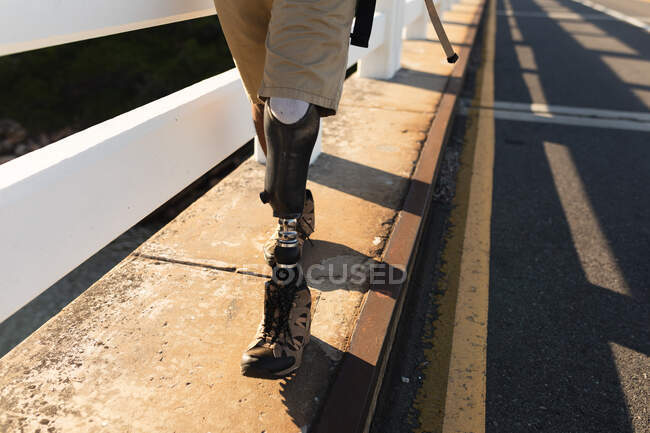 Low section of disabled male athlete with prosthetic leg, enjoying his time on a trip to the mountains, hiking on the road. Active lifestyle with disability. — Stock Photo