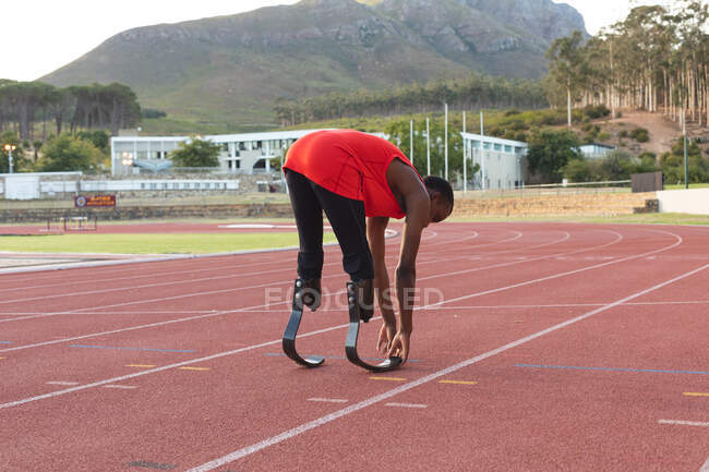 Fit, mixed race disabled male athlete at an outdoor sports stadium, on race track warming up before a race stretching wearing running blades. Disability athletics sport training. — Stock Photo
