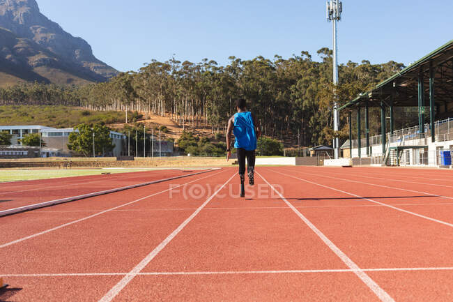 Fit, mixed race disabled male athlete at an outdoor sports stadium, running on race track wearing running blades. Disability athletics sport training. — Stock Photo