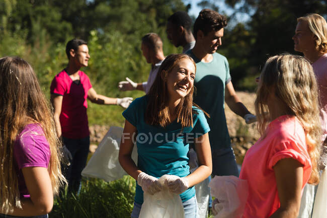 Grupo multiétnico de voluntarios de conservación limpiando el río en el campo, hablando y sonriendo. Ecología y responsabilidad social en el medio rural. - foto de stock