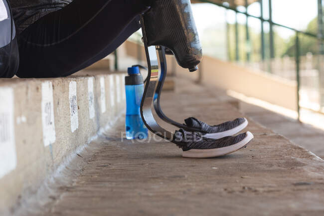 Sezione bassa di atleta di sesso maschile disabile in uno stadio sportivo all'aperto, seduto sugli spalti con le lame da corsa. Disabilità atletica allenamento sportivo. — Foto stock