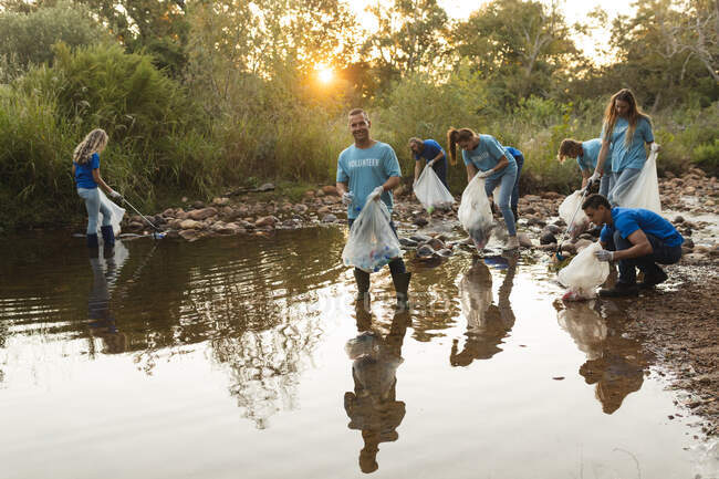 Grupo multiétnico de voluntarios de conservación limpiando el río en el campo, recogiendo basura. Ecología y responsabilidad social en el medio rural. - foto de stock