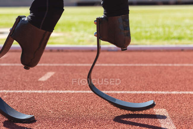 Low section section of fit, disabled male athlete at an outdoor sports stadium, running on race track wearing running blades. Disability athletics sport training. — Stock Photo