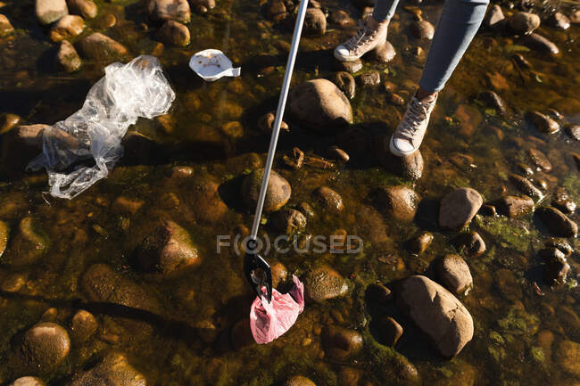 Low section of female conservation volunteer cleaning up river in the countryside, picking up rubbish with grabber. Ecology and social responsibility in rural environment. — Stock Photo