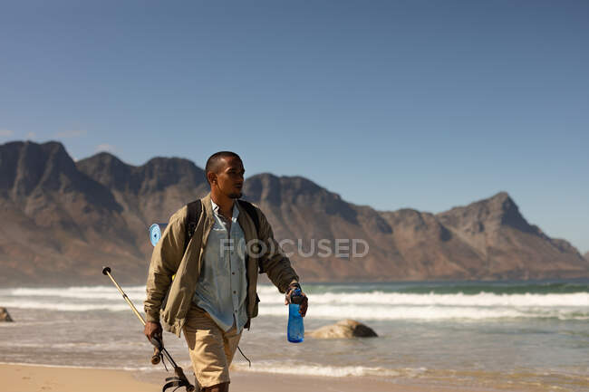 A fit, disabled mixed race male athlete with prosthetic leg, enjoying his time on a trip to the mountains, hiking with sticks, walking on the beach by the sea. Active lifestyle with disability. — Stock Photo