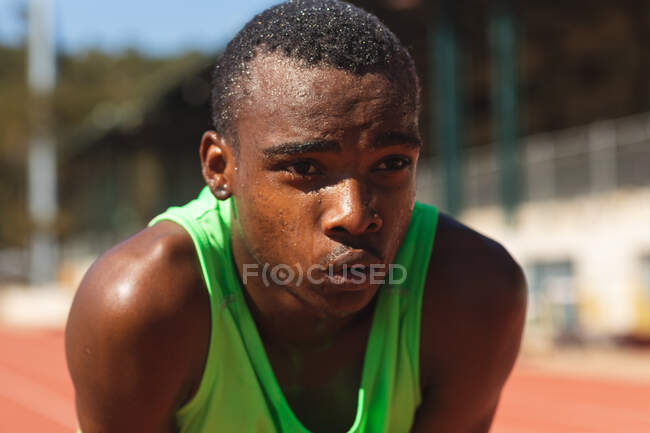 Close up of fit, focused mixed race male athlete at an outdoor sports stadium, on race track after race breathing and resting. Athletics sport training. — Stock Photo