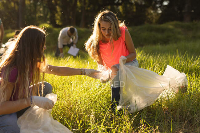 Duas voluntárias caucasianas felizes da conservação com sacos de lixo limpando a floresta no campo, pegando lixo. Ecologia e responsabilidade social no meio rural. — Fotografia de Stock