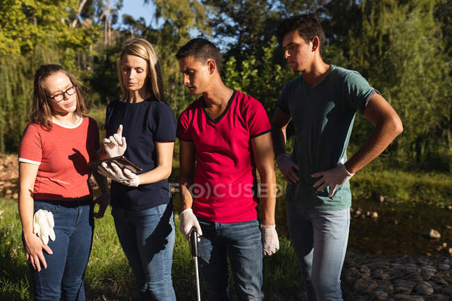 Multi ethnic group of conservation volunteers cleaning up river in the countryside, woman using digital tablet. Ecology and social responsibility in rural environment. — Stock Photo
