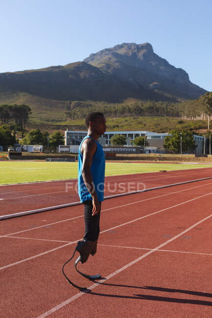 Fit, mixed race disabled male athlete at an outdoor sports stadium, concentrating before workout standing on race track wearing running blades. Disability athletics sport training. — Stock Photo
