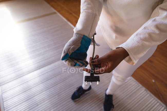 Sportswoman wearing protective fencing outfit during a fencing training session, preparing for a duel, putting glove and body cord on. Fencers training at a gym. — Stock Photo