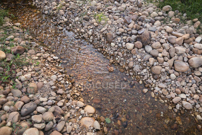 High angle view of river with rocks and surrounded by grass on a sunny day in the countryside. Ecology and social responsibility in a rural environment. — Stock Photo