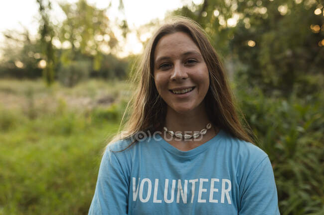 Retrato de la feliz mujer caucásica voluntaria de conservación limpiando el bosque en el campo, sonriendo a la cámara. Ecología y responsabilidad social en el medio rural. - foto de stock