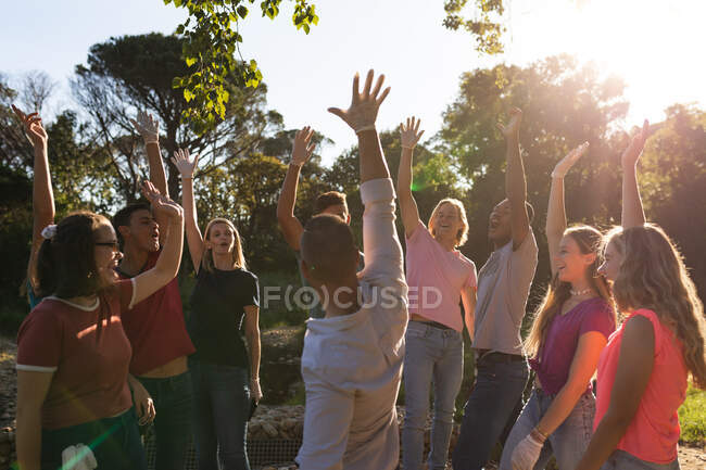 Grupo multiétnico de voluntarios felices de la conservación limpiando río arriba en el campo, sonriendo y chocando los cinco. Ecología y responsabilidad social en el medio rural. - foto de stock