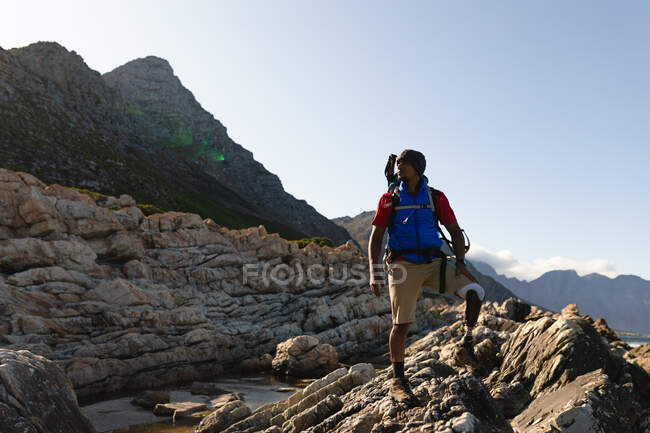 A fit, disabled mixed race male athlete with prosthetic leg, enjoying his time on a trip to the mountains, hiking, admiring the view. Active lifestyle with disability. — Stock Photo