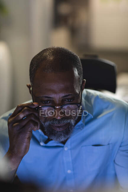 Афроамериканський бізнесмен працює пізно ввечері в сучасному офісі, сидячи за столом, за допомогою настільного комп 