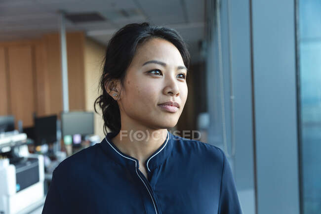 Großaufnahme einer asiatischen Geschäftsfrau, die spät abends in einem modernen Büro arbeitet, durch ein Fenster blickt und denkt. — Stockfoto