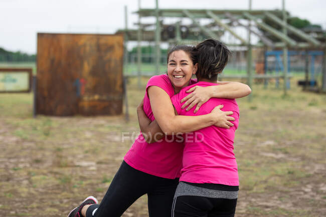 Mujeres de raza mixta que usan camisetas rosas en una sesión de entrenamiento de campo de entrenamiento, ejercitándose, motivándose, abrazándose. Ejercicio en grupo al aire libre, divertido desafío saludable. - foto de stock