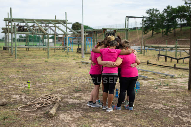 Gruppo multietnico di donne che indossano tutte magliette rosa durante una sessione di allenamento al campo di addestramento, esercitandosi, motivando, abbracciandosi in un gruppo. Esercizio di gruppo all'aperto, divertente sfida sana. — Foto stock