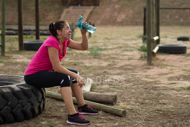 A Caucasian woman wearing pink t shirt at a boot camp training session, exercising, taking a break, pouring water on her face. Outdoor group exercise, fun healthy challenge. — Stock Photo