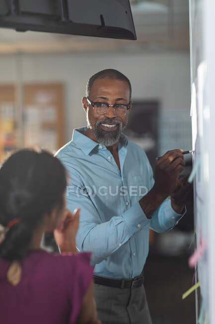 African American businessman and Asian businesswoman working late in the evening in a modern office, writing on a moodboard and brainstorming. — Stock Photo
