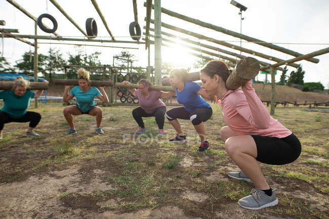 Gruppo multietnico di donne che indossano magliette colorate in una sessione di allenamento del campo di addestramento, esercitandosi, trasportando tronchi. Esercizio di gruppo all'aperto, divertente sfida sana. — Foto stock