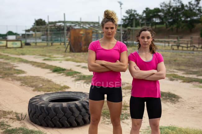 Portrait de femmes caucasiennes confiantes dans un camp d'entraînement, portant un t-shirt rose avec les bras croisés, un pneu en arrière-plan. Exercice de groupe en plein air, défi sain amusant. — Photo de stock