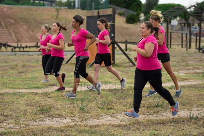 Groupe multiethnique de femmes portant toutes des t-shirts roses lors d'une séance d'entraînement au camp d'entraînement, faisant de l'exercice, courant sur un terrain. Exercice de groupe en plein air, défi sain amusant. — Photo de stock