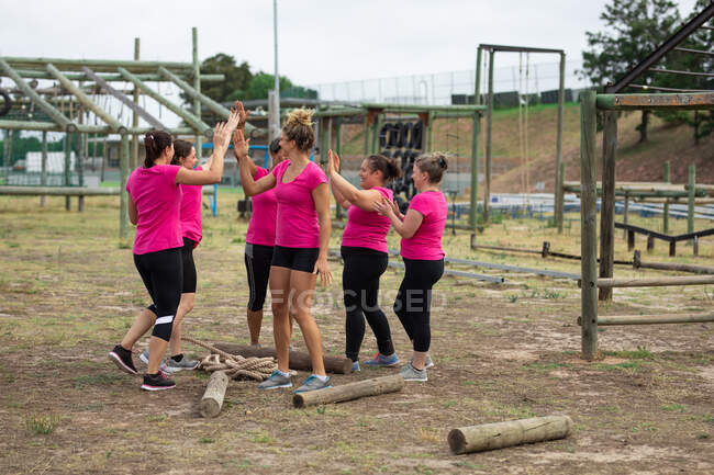 Багатоетнічна група жінок носять рожеві футболки на тренувальній сесії табору, займаються спортом, мотивують один одного, даючи п'ять. На відкритому повітрі група вправи, весело здоровий виклик . — стокове фото